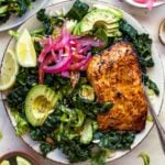 A plate of greens topped with sliced avocado, pickled red onion, and salmon fillet.