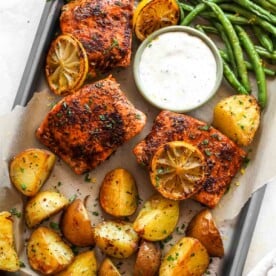 Salmon, roasted potatoes, green beans, and herb sauce on a silver baking sheet as part of a spring dinner recipe collection.