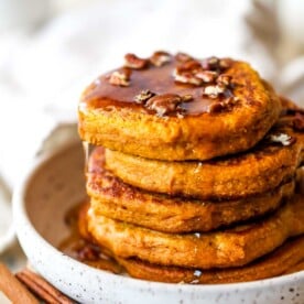 Stack of pumpkin pancakes topped with pecans and maple syrup