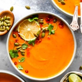 Creamy Thai Pumpkin Soup in a grey bowl topped with cilantro and lime