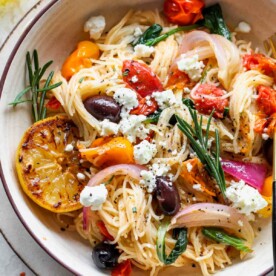 Angel hair spaghetti in a bowl with cherry tomatoes, rosemary, and olives.