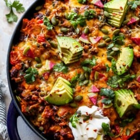 Skillet pumpkin enchiladas topped with avocado and cilantro