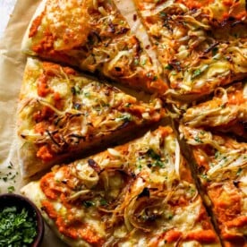 Pumpkin and gouda pizza being sliced on a piece of parchment paper