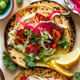 Salmon tacos with garnishes on a white platter.