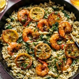 Lemon pepper shrimp and orzo in a cast iron skillet topped with lemon slices