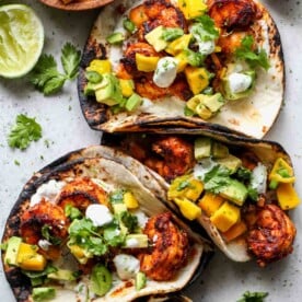 Chipotle shrimp tacos arranged on a surface with lime crema and mango salsa