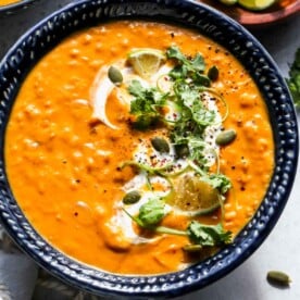 Blue bowl filled with pumpkin red lentil soup topped with herbs and pepitas