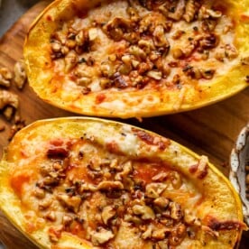 Pumpkin pasta sauce filled spaghetti squash topped with walnuts on a cutting board