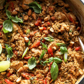 Thai chicken and quinoa in a white pan topped with lime wedges and basil leaves