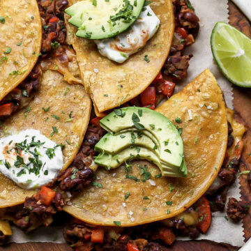 Crispy black bean tacos topped with sour cream, avocado, and cilantro arranged on a wooden serving platter.