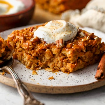One square of baked pumpkin oats on a white plate topped with a dollop of yogurt.