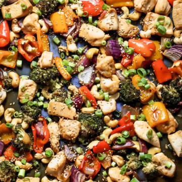 Sheet pan honey-sesame chicken and veggies mixed together on a blue baking sheet.