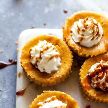 Mini pumpkin cheesecakes with whipped topping arranged on a white serving platter.
