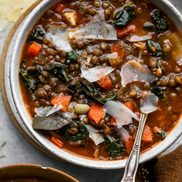 A small white soup bowl filled with lentil soup and Parmesan. Styled on a grey surface.