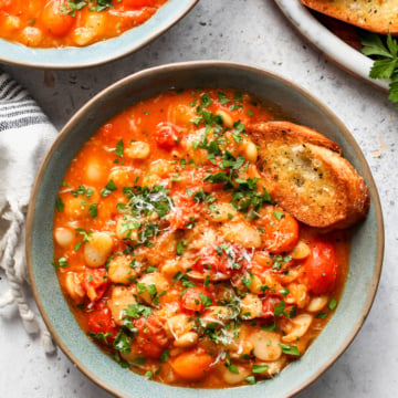 Tomato and butter bean stew styled in a blue bowl topped with parsley and Parmesan.