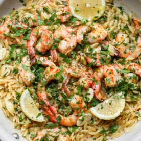 Shrimp scampi orzo styled in a white skillet with lemon wedges as garnish.