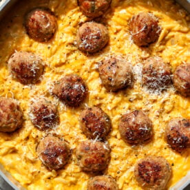 Sage turkey meatballs arranged in a skillet of pumpkin orzo topped with Parmesan.