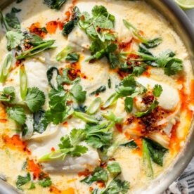 Coconut Poached Fish styled in a large skillet topped with cilantro, scallions, and chili oil.