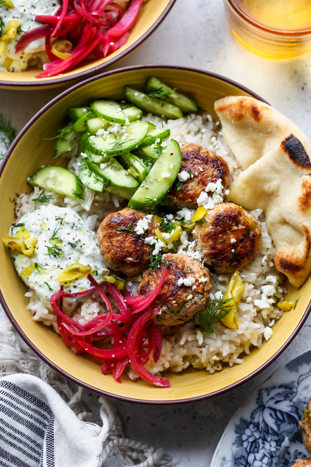 Peperoncini-Feta Turkey Meatballs styled in a yellow bowl with rice, cucumbers, pita, and pickled red onion.