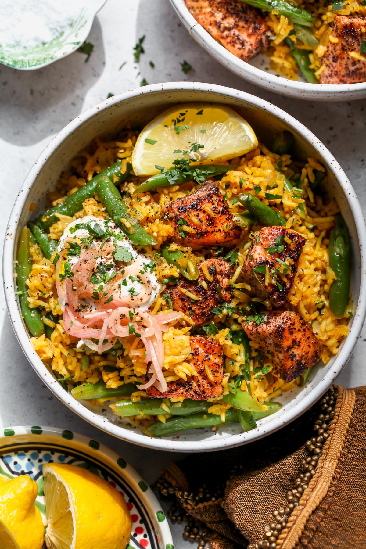 Sumac Salmon with Golden Rice and green beans styled in a white bowl topped with a dollop of yogurt and pickled shallots.
