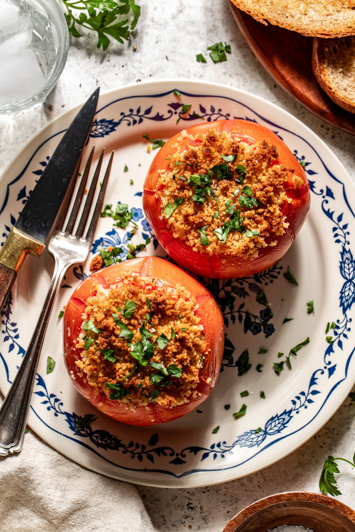 Two Baked Stuffed Tomatoes arranged on a blue and white plate with a fork resting on the left side.