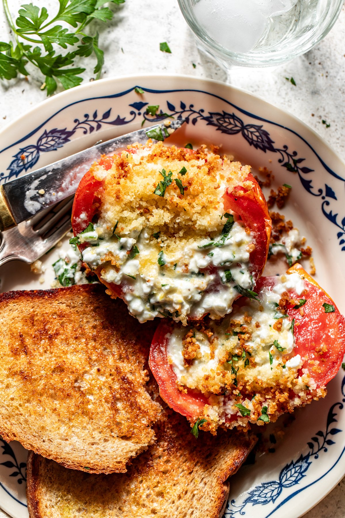 One baked stuffed tomato sliced in half on a plate to show the inside filling.