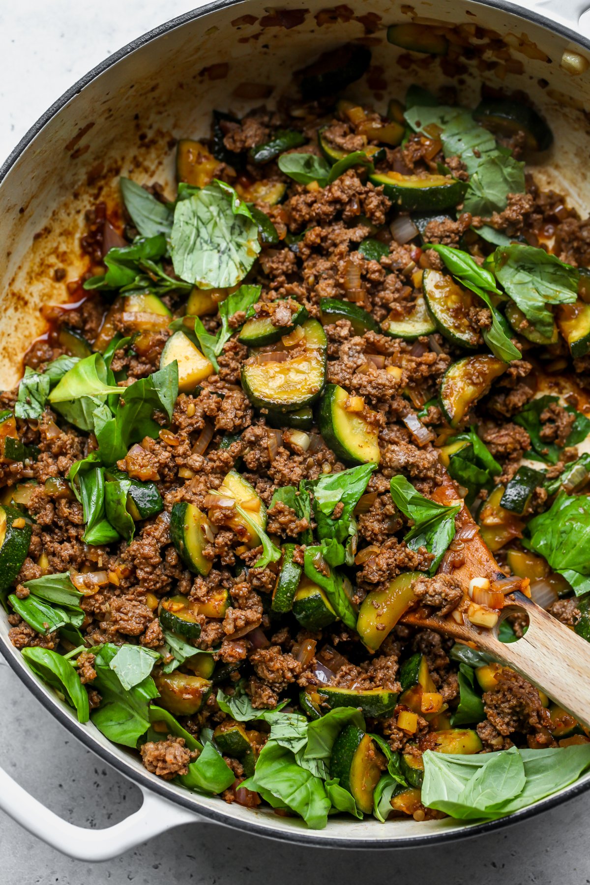 Fresh basil leaves being mixed into a saucy skillet of beef and zucchini.