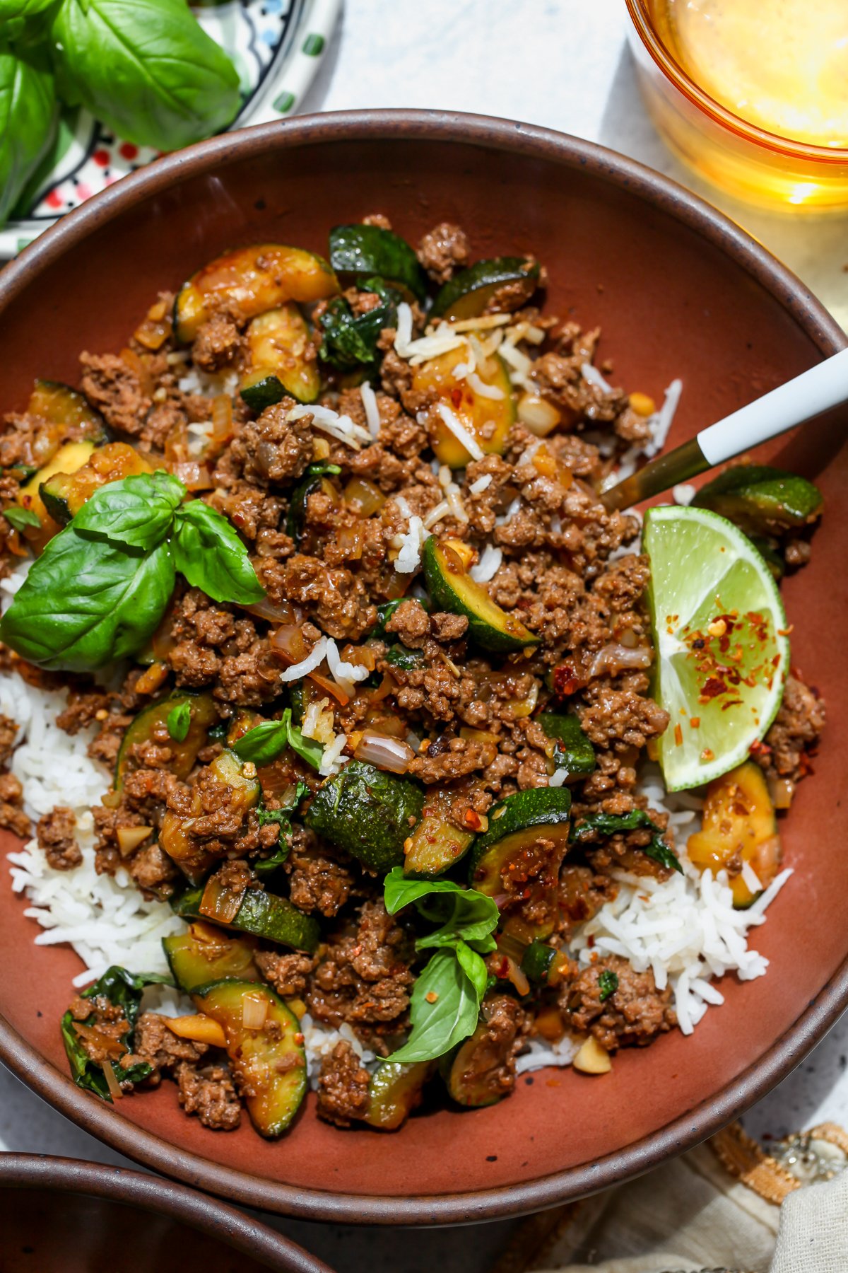 Beef and zucchini served over rice in a maroon bowl topped with fresh basil leaves.