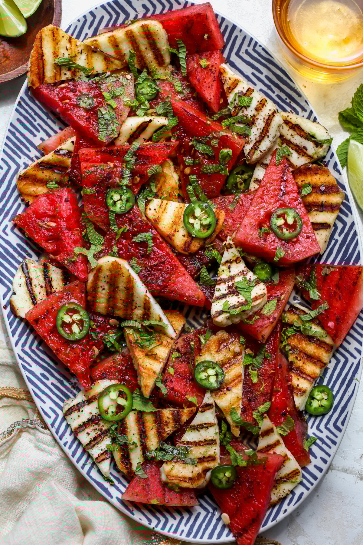 Grilled halloumi and watermelon salad arranged on a blue and white platter topped with jalapeño, mint, and sumac.