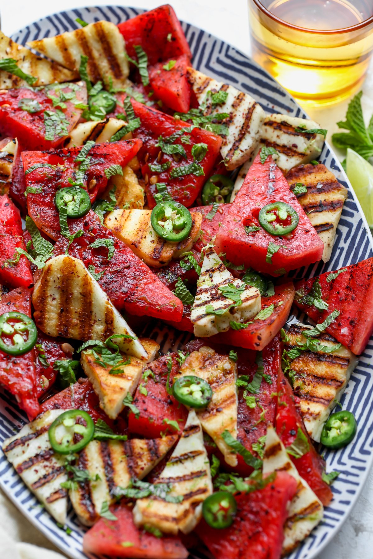 Halloumi watermelon salad styled on a platter topped with jalapeño slices, fresh mint, and ground sumac.
