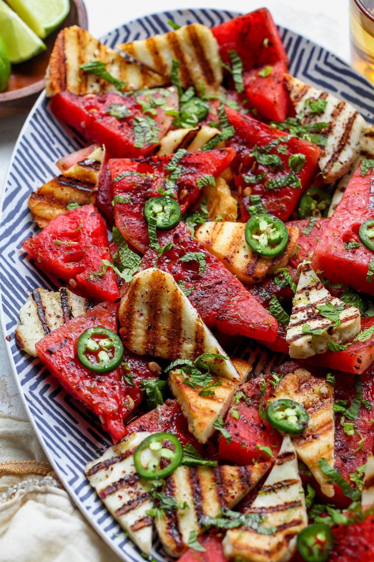 Grilled halloumi cheese and watermelon chunks arranged on a blue and white striped platter with honey-lime dressing overtop.