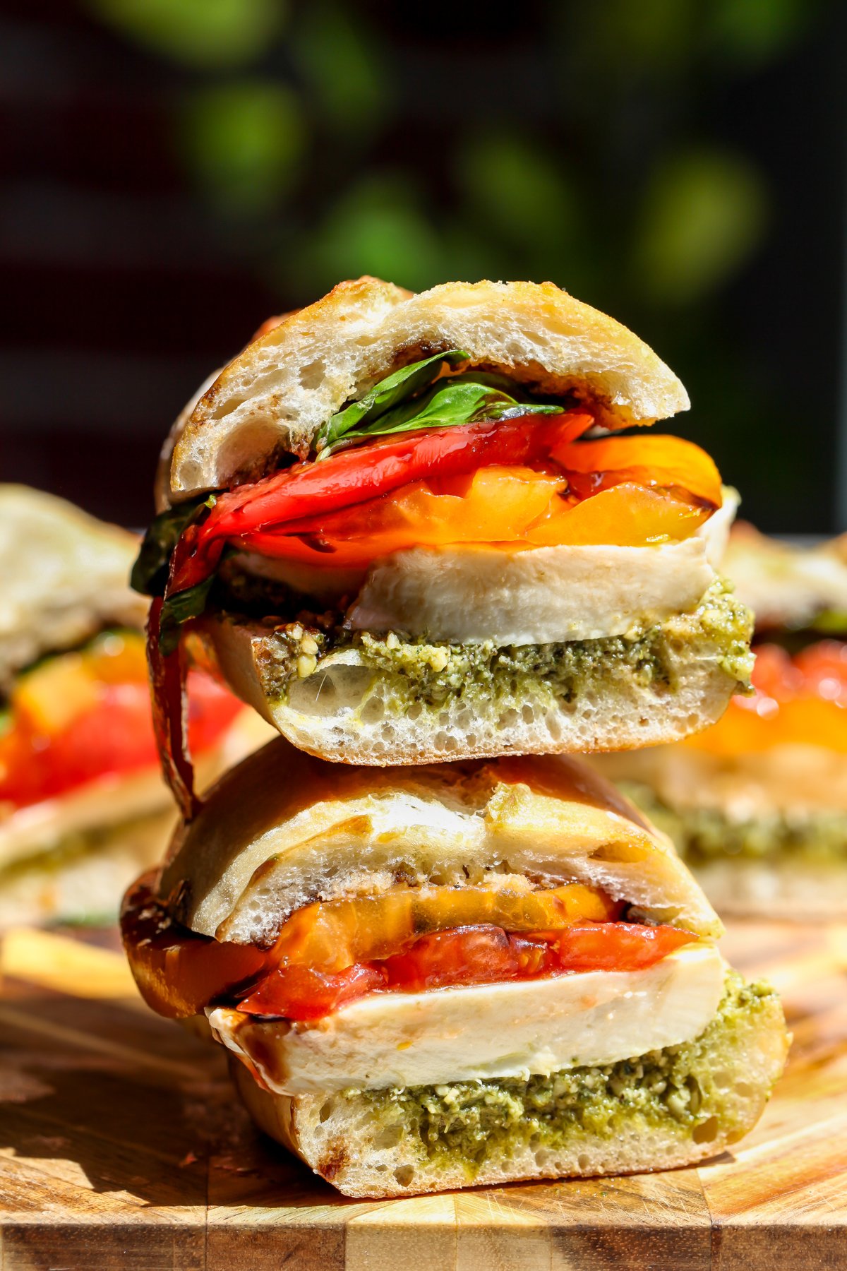 A sliced pesto caprese sandwich stacked on top of one another on a cutting board as part of a collection of no cook lunch ideas.