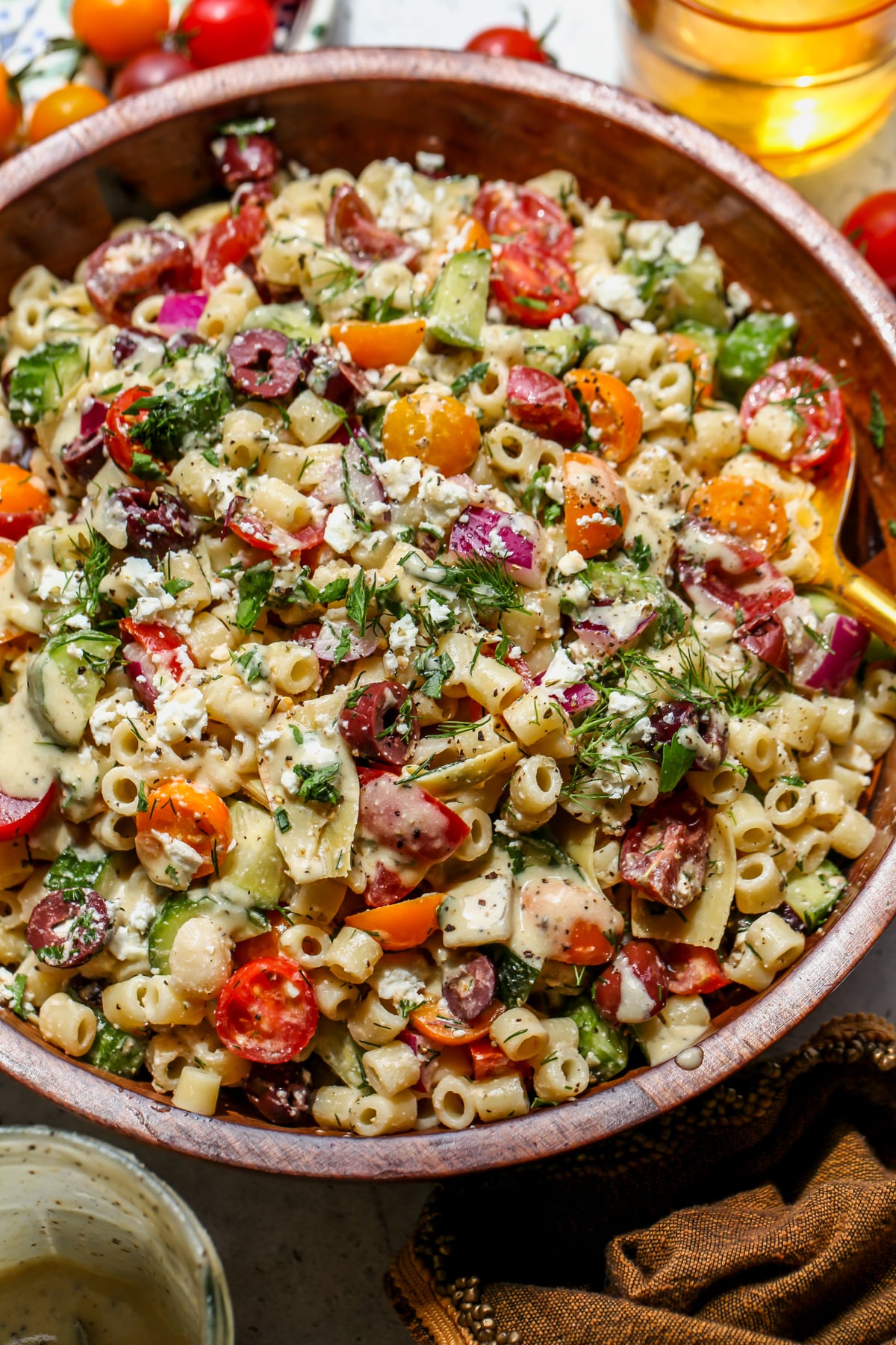 Chopped greek pasta salad styled in a wooden serving bowl with a spoon resting on the right side.