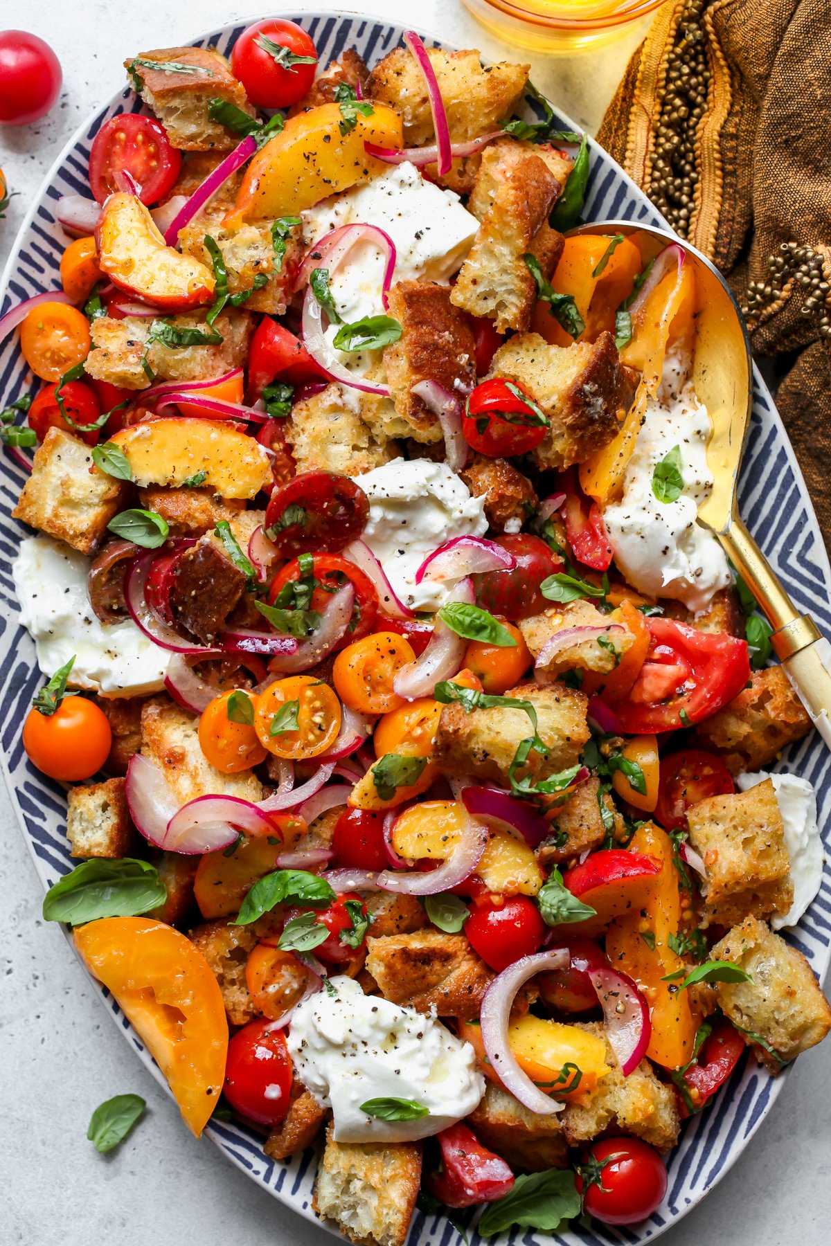 Summer panzanella salad assembled on a white and blue tray with a serving spoon resting on the right side.