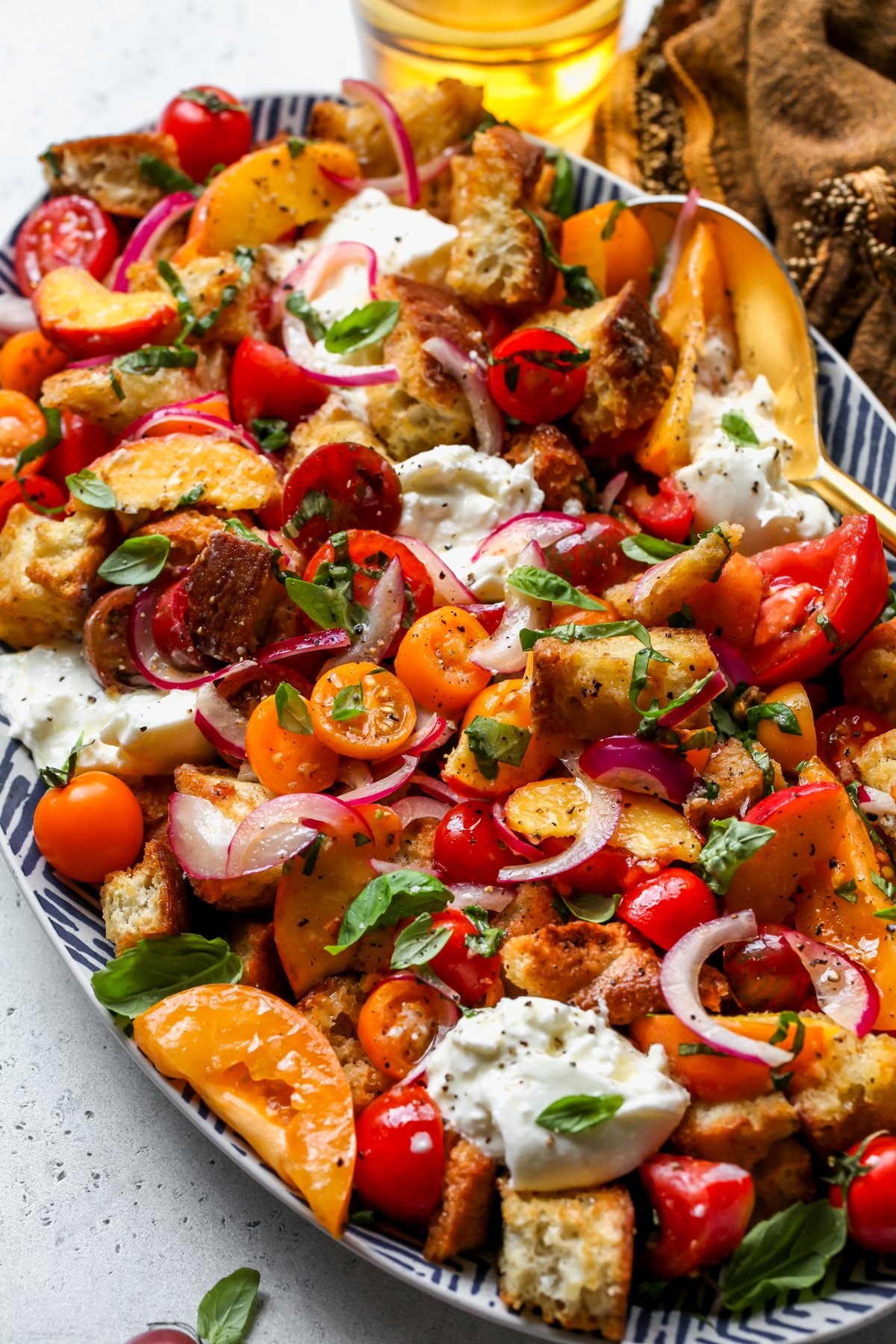 Summer Panzanella Salad styled on a white and blue platter with a serving spoon resting on the right side.