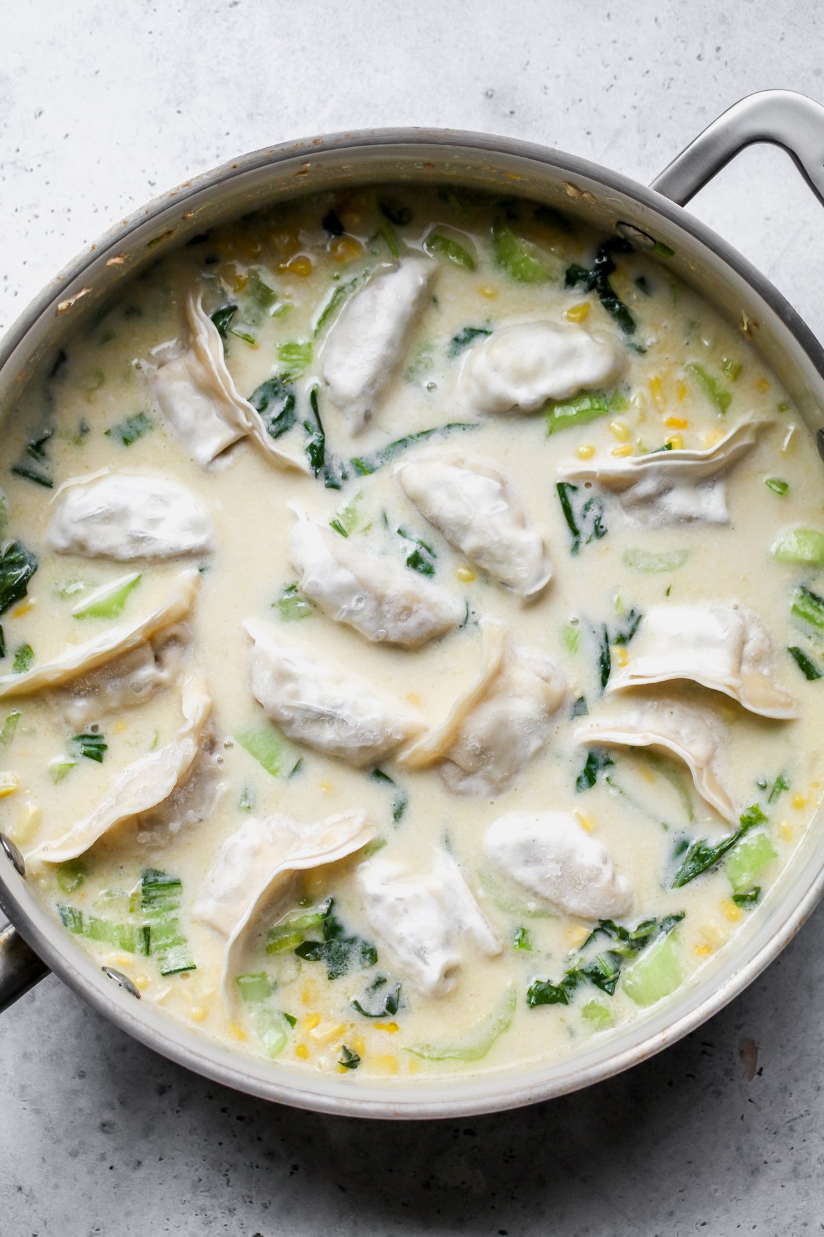 Frozen potstickers added to a pan of sweet corn coconut broth.