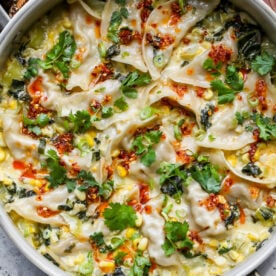 One pan dumplings arranged in a saut&eacute; pan topped with chili crisp, scallions, and cilantro.