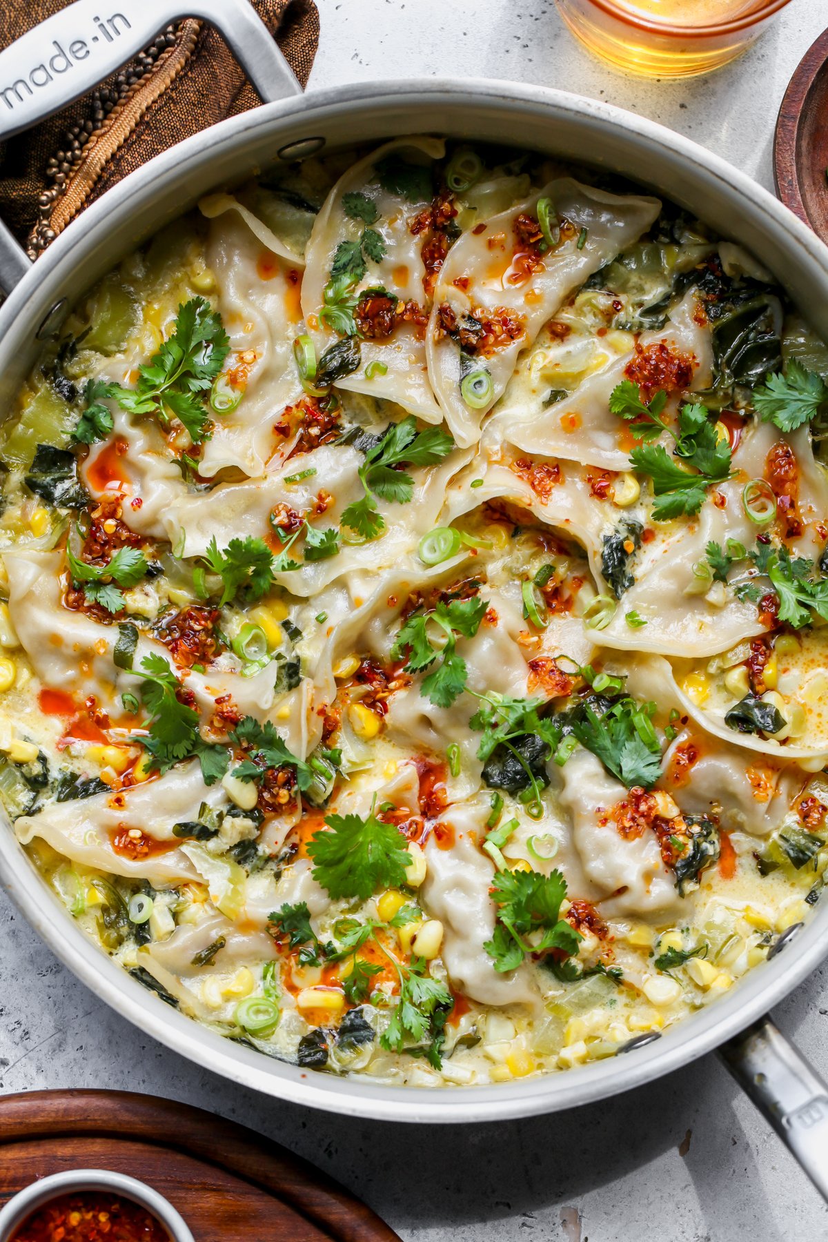 One pan dumplings arranged in a sauté pan topped with chili crisp, scallions, and cilantro.