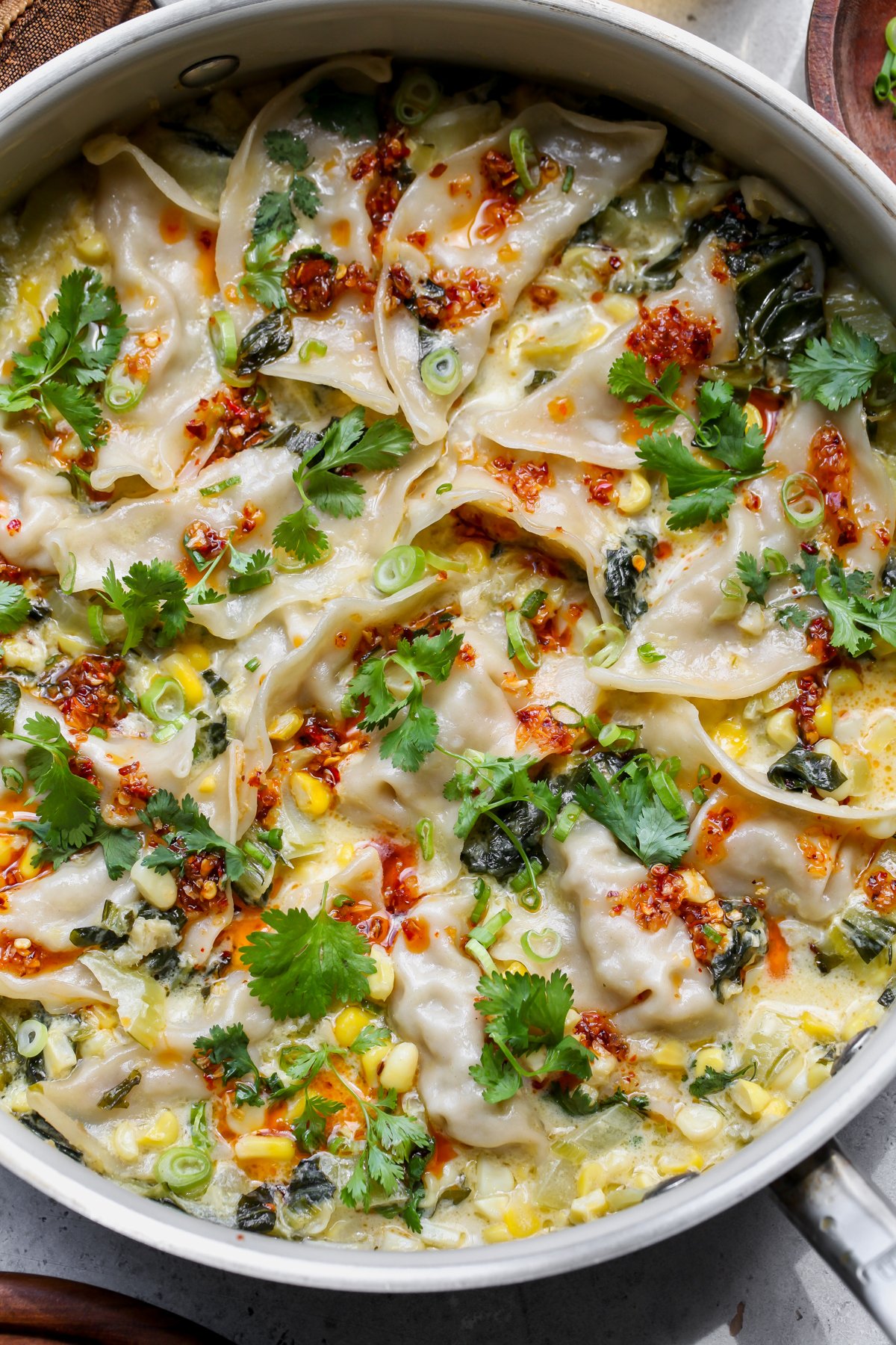 One pan dumplings styled in a white sauté pan topped with fresh herbs and chili crunch.