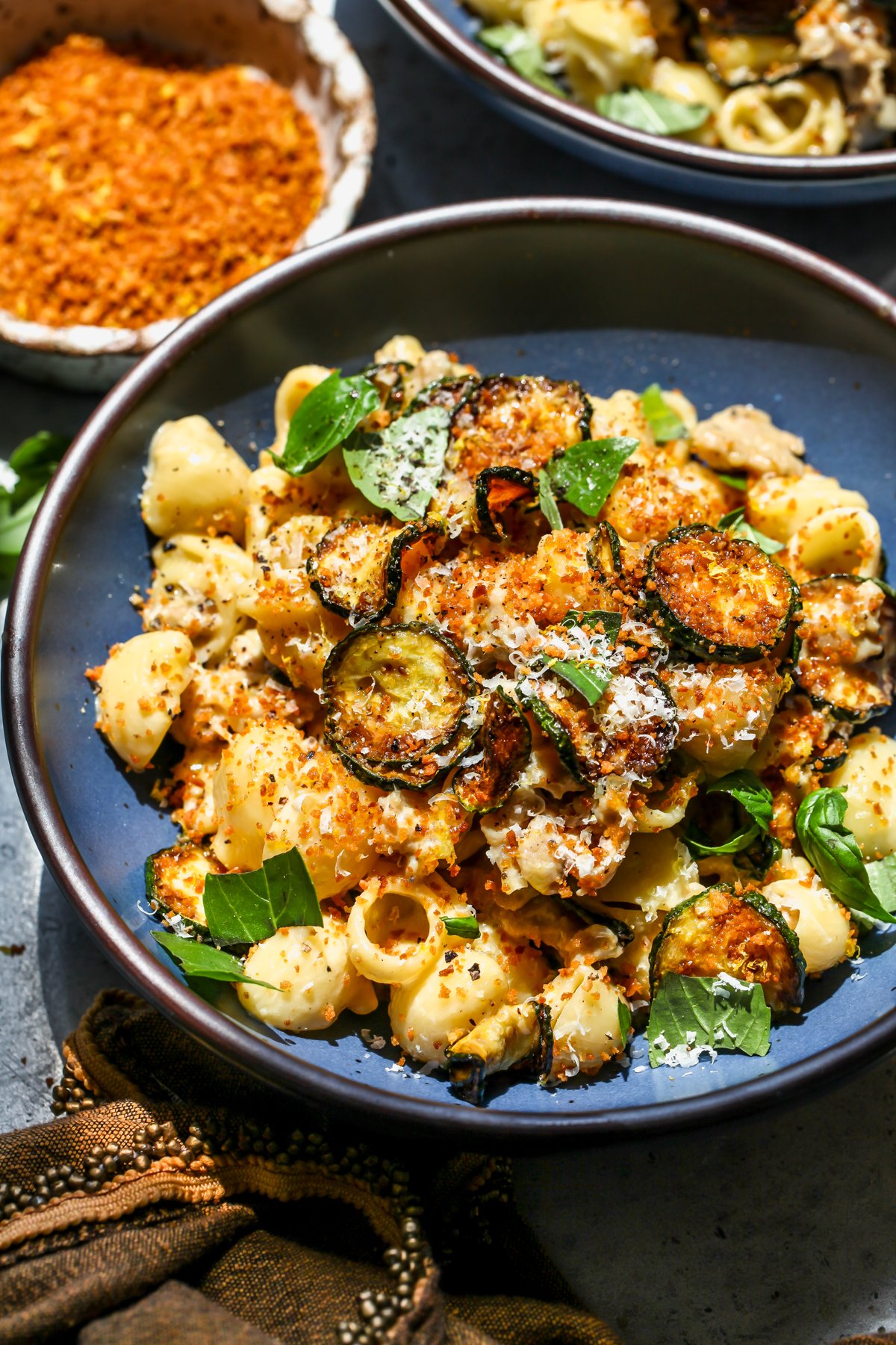 Zucchini and sausage pasta styled in a blue pasta bowl next to a bowl of breadcrumbs.