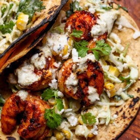 Easy shrimp taco topped with cilantro, crumbled cheese, and creamy salsa verde styled on a wooden serving platter.