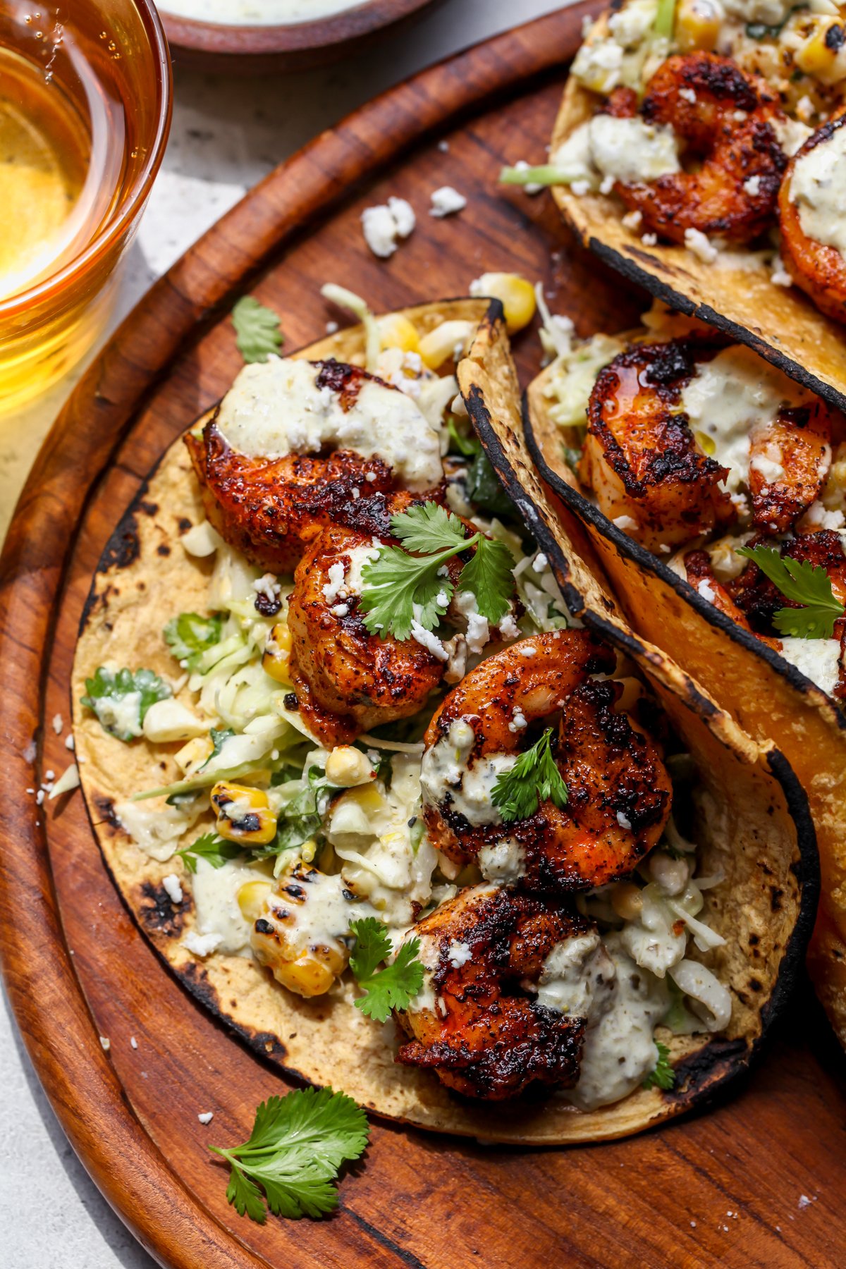Easy Shrimp Tacos arranged on a wooden board topped with cilantro and creamy salsa verde sauce.