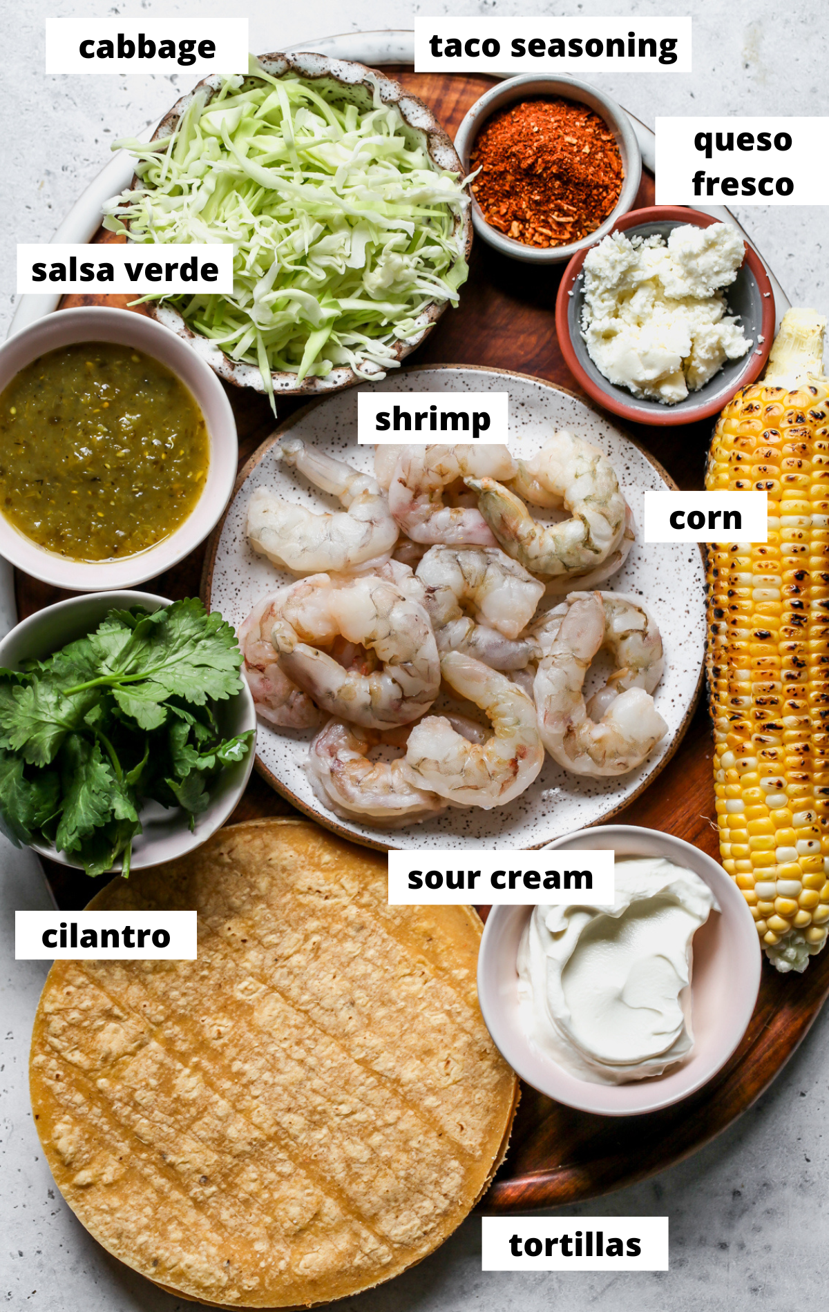 Recipe ingredients arranged in separate bowls with labels on a wooden platter.