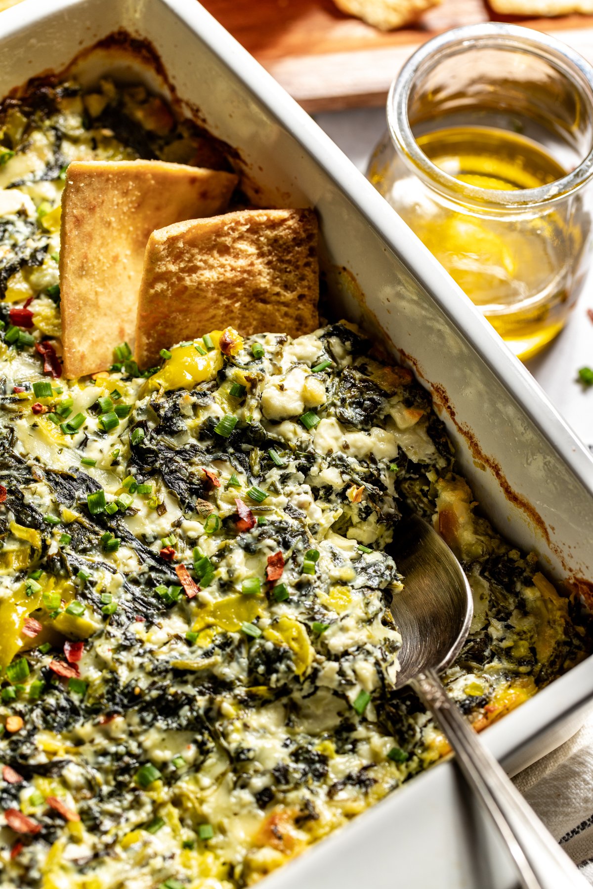 Pita chips scooping a portion of baked feta dip out of a baking dish.