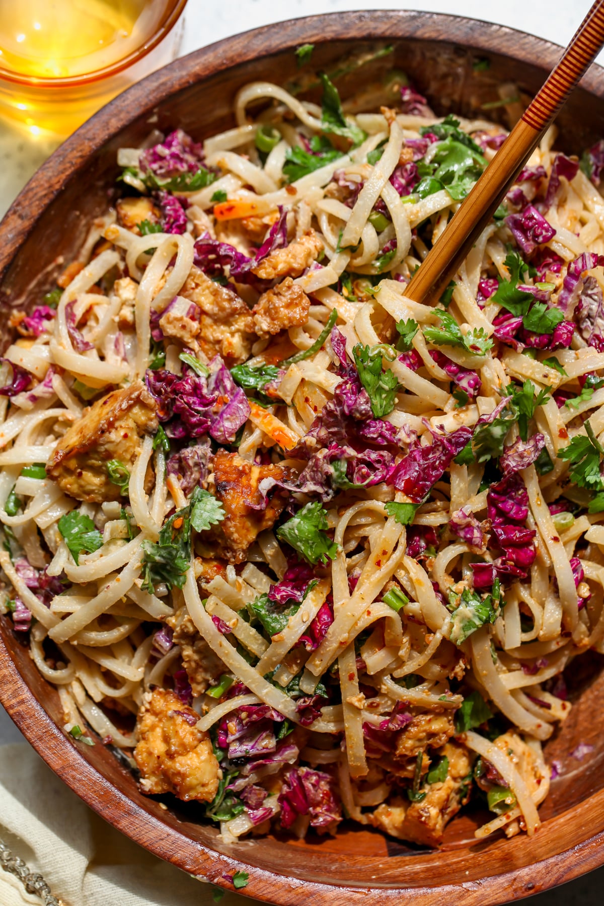 Chilled noodle salad being tossed with a set of chopsticks in a large wooden serving bowl.