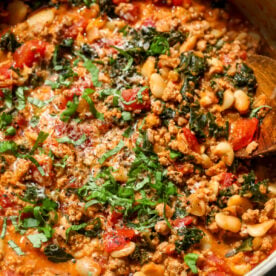Tuscan Turkey and White Bean Skillet topped with fresh basil leaves and Parmesan styled in a white saut&eacute; pan.