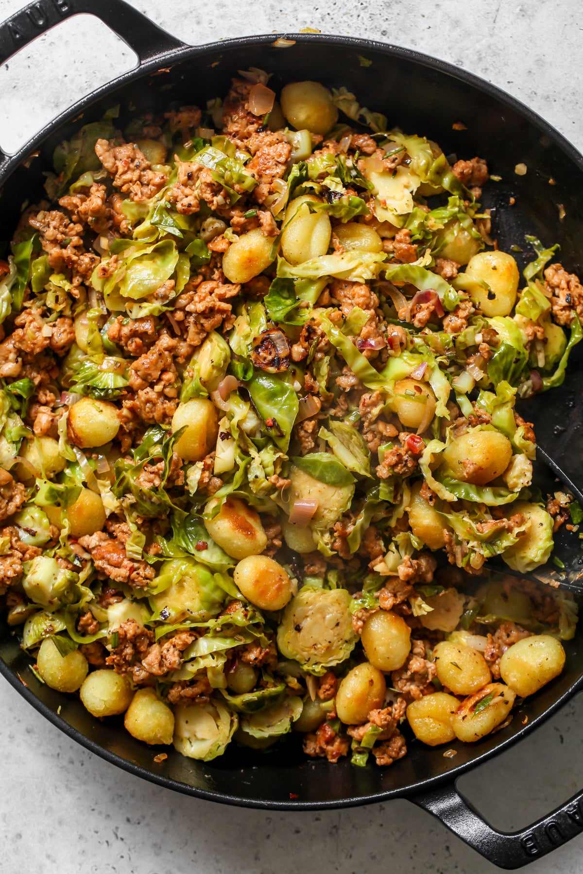 A black cast iron skillet filled with cooked gnocchi, sausage, and Brussels sprouts dish.