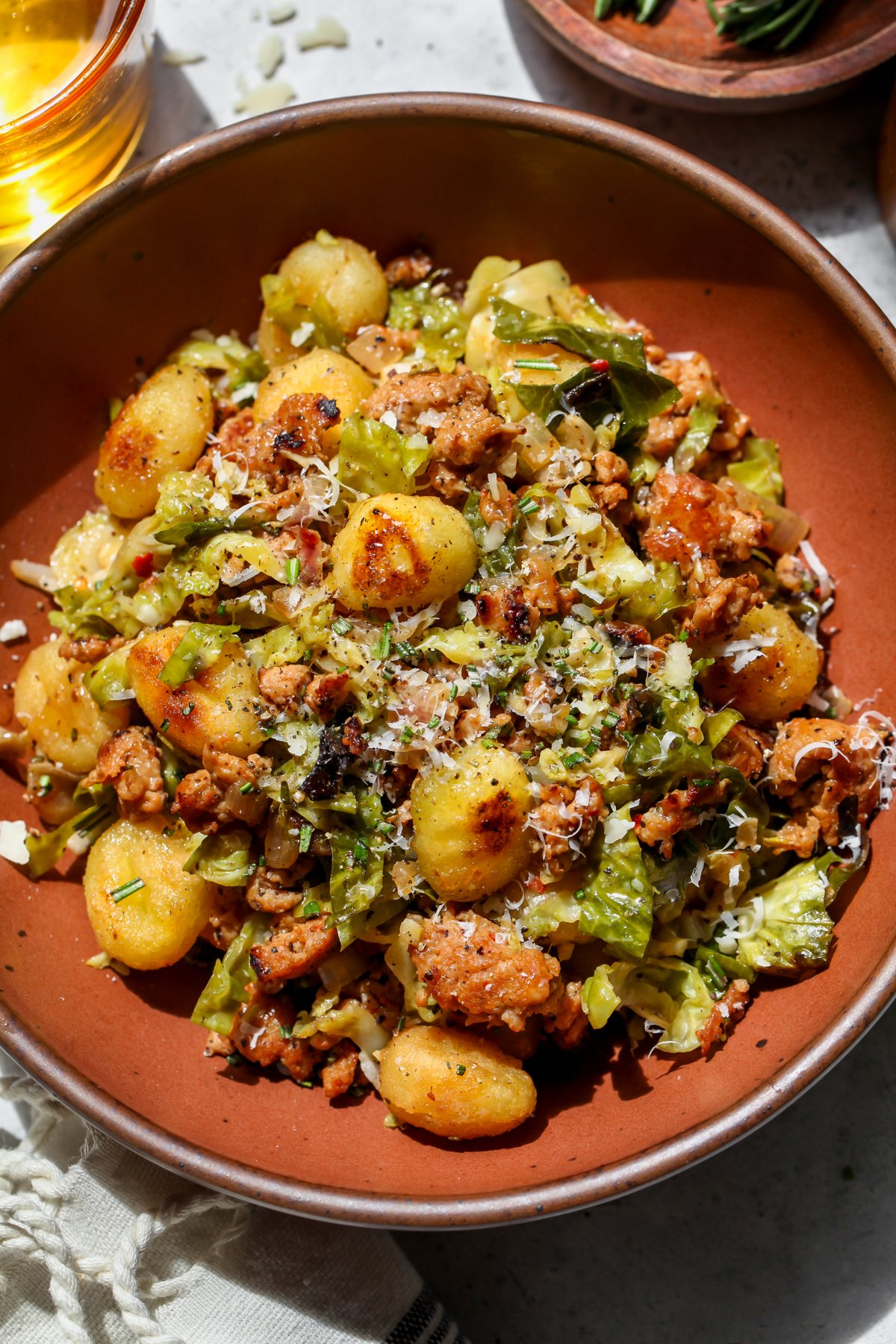 A maroon bowl filled with crispy gnocchi recipe. Garnished with parmesan, black pepper, and rosemary.