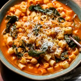 Pasta e Ceci styled in a blue bowl on a wooden tray with a spoon resting on the right side.