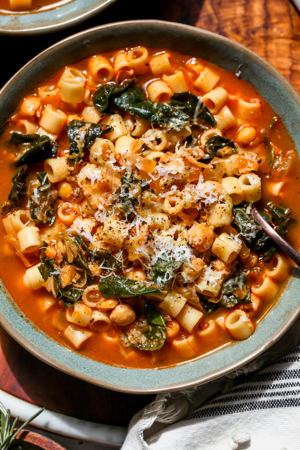 A spoon digging into a bowl of pasta e ceci. Styled on a wooden serving platter.